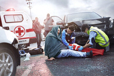 Rescue workers preparing vacuum leg splint on car accident victim in road - CAIF13119