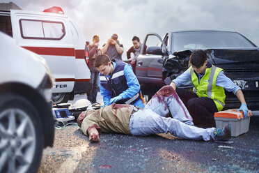 Rescue workers tending to bloody car accident victim in road - CAIF13131