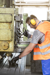 Arbeiter in Arbeitsschutzkleidung bei der Bedienung von Maschinen in einer Fabrik - CAIF13149