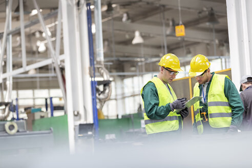 Arbeiter in Arbeitsschutzkleidung im Gespräch mit der Zwischenablage in einer Fabrik - CAIF13153