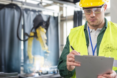 Arbeiter in Arbeitsschutzkleidung mit Klemmbrett in einer Fabrik - CAIF13155