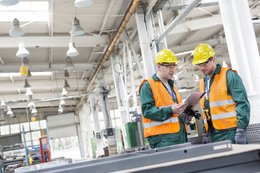 Arbeiter in Arbeitsschutzkleidung mit Klemmbrett in einer Fabrik - CAIF13164