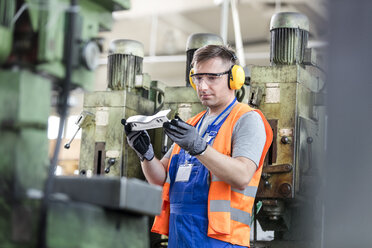 Arbeiter in Arbeitsschutzkleidung bei der Prüfung eines Teils in einer Fabrik - CAIF13167