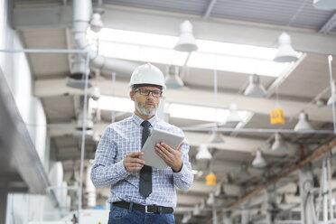 Engineer with hard-hat and digital tablet walking in factory - CAIF13170