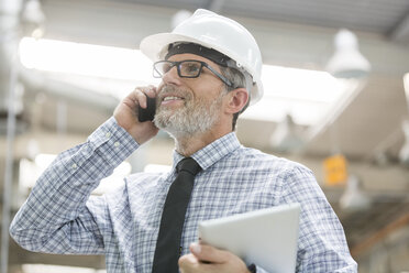 Ingenieur mit Schutzhelm und digitalem Tablet, der mit einem Handy telefoniert - CAIF13172