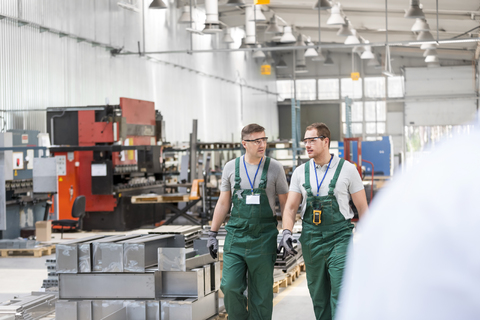 Arbeiter gehen und sprechen in einer Fabrik, lizenzfreies Stockfoto