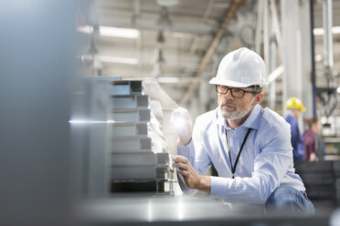 Ingenieur, der in einer Fabrik Stahlteile mit einer Taschenlampe untersucht - CAIF13176