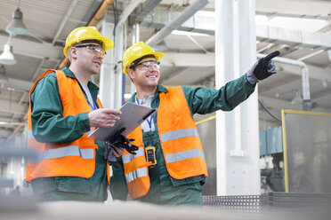 Arbeiter in Arbeitsschutzkleidung im Gespräch mit Klemmbrett in einer Fabrik - CAIF13182