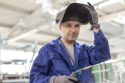 Porträt eines selbstbewussten Schweißers mit Schweißbrenner in einer Fabrik - CAIF13183