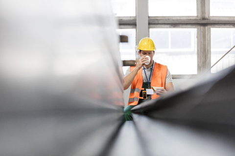 Arbeiter in Arbeitsschutzkleidung trinkt Kaffee in einer Fabrik, lizenzfreies Stockfoto