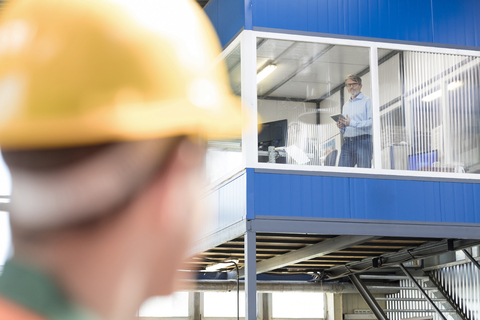 Arbeiter blickt zu Geschäftsmann in Fabrikbüro auf, lizenzfreies Stockfoto