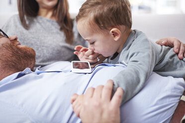 Curious toddler looking at cell phone on father’s chest - CAIF13215