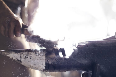 Nahaufnahme eines Schmieds, der ein Eisenwerkzeug über einen Amboss in einer Schmiede bürstet - CAIF13253