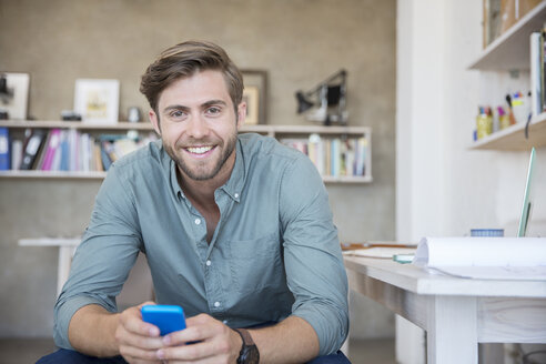 Porträt eines jungen blonden Mannes, der mit einem Mobiltelefon sitzt - CAIF13307