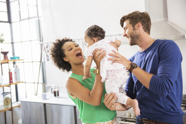 Happy parents holding their baby daughter in domestic kitchen - CAIF13314