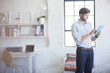 Man with digital tablet standing in home office - CAIF13318