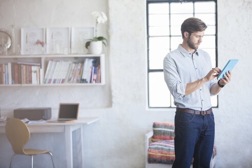 Mann mit digitalem Tablet im Home Office stehend - CAIF13318