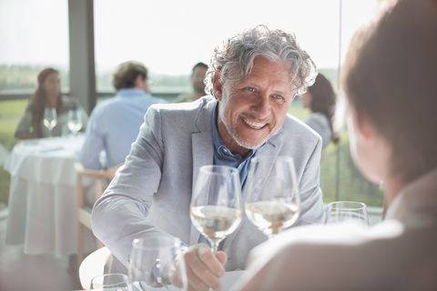 Lächelndes Paar trinkt Wein in einem sonnigen Restaurant, lizenzfreies Stockfoto