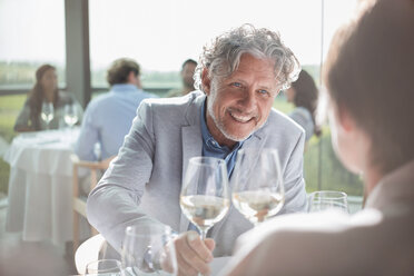 Lächelndes Paar trinkt Wein in einem sonnigen Restaurant - CAIF13353