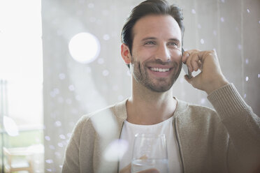 Lächelnder Mann, der Wasser trinkt und mit einem Handy telefoniert - CAIF13362