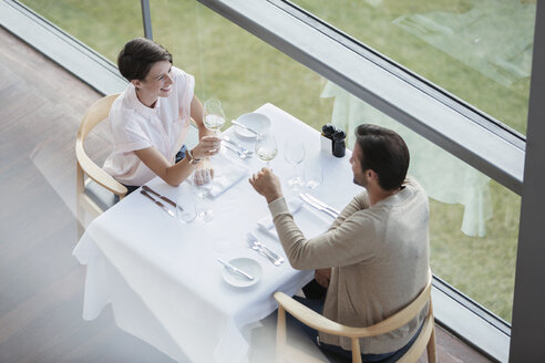 Ehepaar stößt mit Weingläsern am Restauranttisch am Fenster an - CAIF13368
