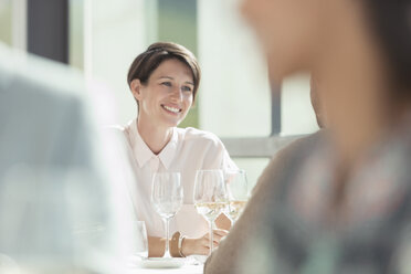 Lächelnde Frau trinkt Weißwein in einem sonnigen Restaurant - CAIF13374