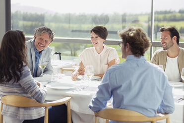 Freunde trinken Weißwein und unterhalten sich am sonnigen Restauranttisch - CAIF13375