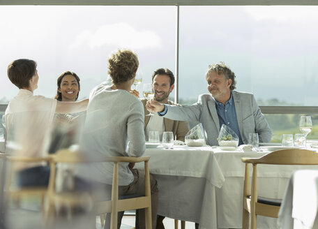 Freunde stoßen mit Weingläsern am sonnigen Restauranttisch an - CAIF13376