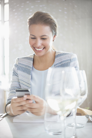 Lächelnde Frau, die mit ihrem Handy am Restauranttisch SMS schreibt, lizenzfreies Stockfoto