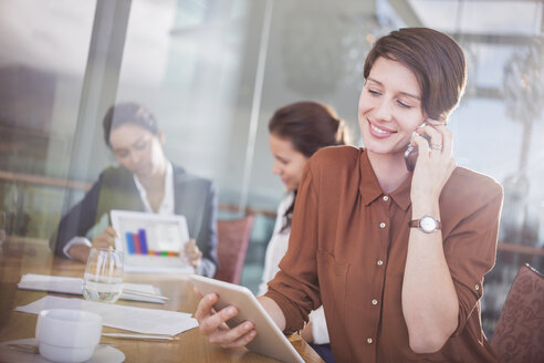 Geschäftsfrau, die mit einem Handy telefoniert und ein digitales Tablet im Büro benutzt - CAIF13390