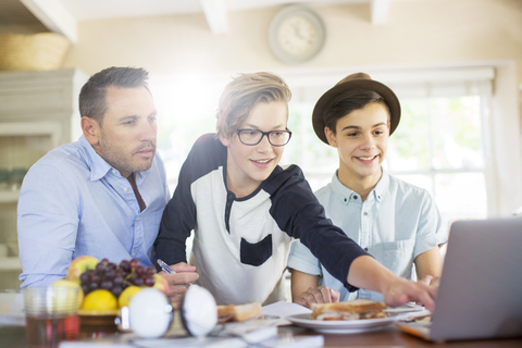 Teenager-Jungen mit Vater benutzen Laptop im Esszimmer, lizenzfreies Stockfoto