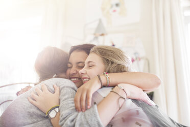 Three teenage girls embracing at home - CAIF13414