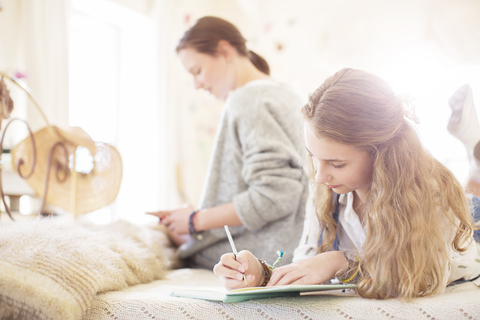 Zwei Teenager-Mädchen auf dem Bett, die in Notizblöcke schreiben, lizenzfreies Stockfoto