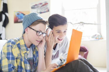 Zwei Teenager teilen sich Laptop und Kopfhörer im Zimmer - CAIF13427