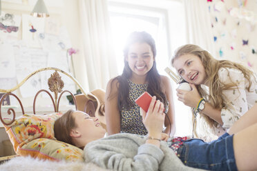 Three teenage girls listening to music from smartphone in bedroom - CAIF13457