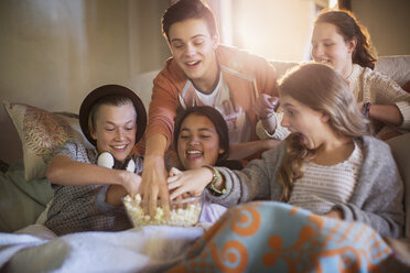 Gruppe von Teenagern isst Popcorn auf dem Sofa im Wohnzimmer - CAIF13465