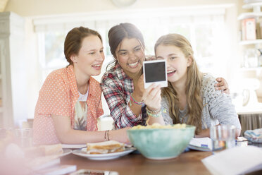 Drei Mädchen im Teenageralter betrachten ein Foto, während sie am Tisch sitzen - CAIF13466