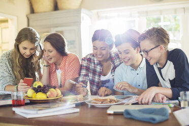 Group of teenagers using electronic devices at table in dining room - CAIF13471