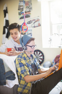 Zwei Teenager benutzen elektronische Geräte im Zimmer - CAIF13476