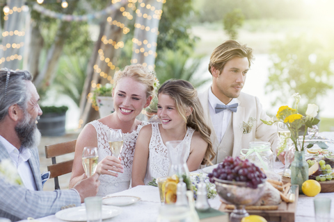 Junges Paar und ihre Gäste sitzen am Tisch während der Hochzeitsfeier im Garten, lizenzfreies Stockfoto