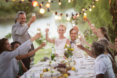 Young couple and their guests toasting with champagne during wedding reception in garden - CAIF13490