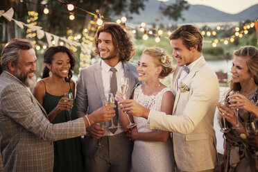 Junges Paar und ihre Gäste mit Sektflöten während der Hochzeitsfeier im Garten - CAIF13495