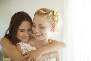 Bridesmaid embracing bride in bedroom - CAIF13505