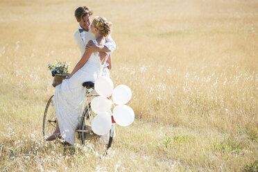 Bride and bridegroom riding bike with balloons attached - CAIF13518