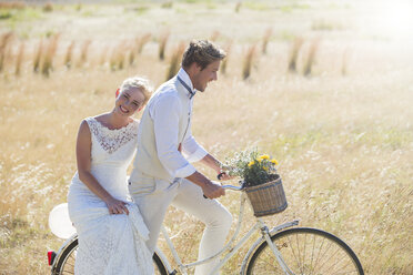 Young couple riding bike in meadow - CAIF13525