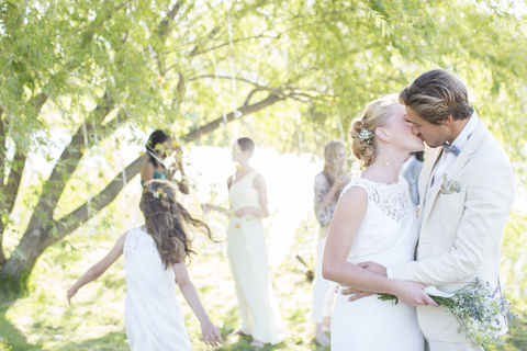 Junges Paar küsst sich beim Hochzeitsempfang im heimischen Garten, lizenzfreies Stockfoto