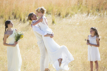 Brautjungfer und Brautjungfer beobachten und lachen, junges Paar umarmt sich auf einer Wiese - CAIF13541