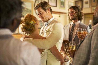 Bräutigam umarmt die Braut während des Hochzeitsempfangs im häuslichen Raum - CAIF13549