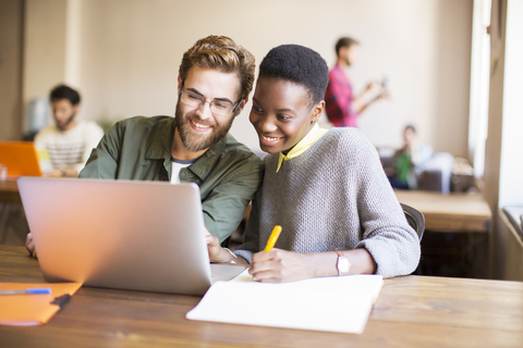 Lächelnde kreative Geschäftsleute mit Laptop und Brainstorming, lizenzfreies Stockfoto