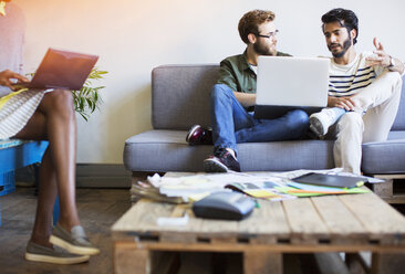 Lässige Geschäftsleute im Gespräch und mit Laptop auf dem Sofa - CAIF13563